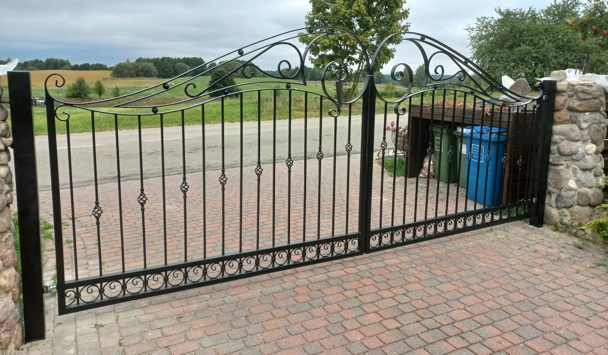 Metalinė tvora su vertikaliais strypais ir dekoratyviniais akcentais – kalvio darbas